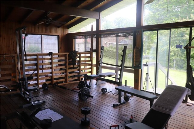 gym with ceiling fan, wooden walls, hardwood / wood-style flooring, and beamed ceiling