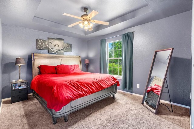carpeted bedroom with a tray ceiling, a textured wall, baseboards, and a ceiling fan
