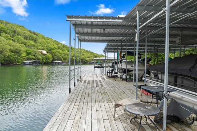 dock area with a water view, boat lift, and a forest view