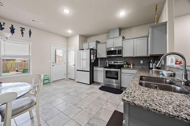 kitchen with stainless steel appliances, a sink, gray cabinets, dark stone countertops, and recessed lighting