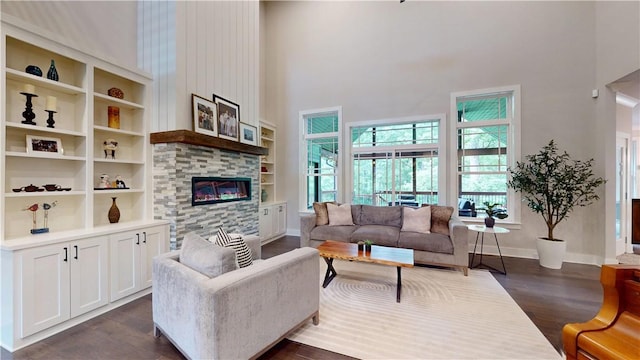 living area featuring a high ceiling, dark wood-style flooring, a stone fireplace, and baseboards