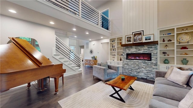 living area featuring wood finished floors, a high ceiling, a glass covered fireplace, stairway, and recessed lighting