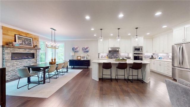 kitchen with stainless steel appliances, under cabinet range hood, a center island, light countertops, and decorative backsplash