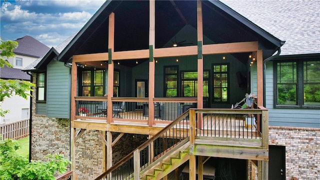 rear view of property featuring brick siding, stairway, a sunroom, and roof with shingles