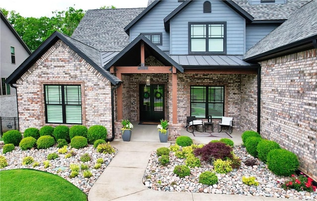 entrance to property featuring brick siding, french doors, roof with shingles, and a standing seam roof