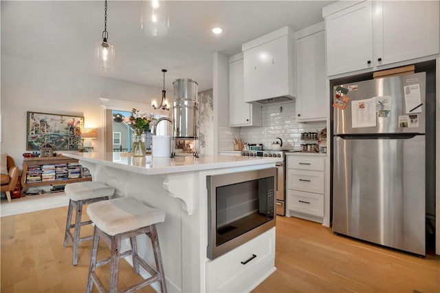 2630 N Gulley Grove Cir, Fayetteville, AR 72703 - kitchen with appliances with stainless steel finishes, decorative backsplash, light wood-style flooring, white cabinets, and a kitchen breakfast bar