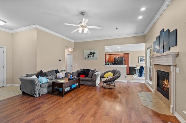 living room featuring a ceiling fan, light wood-type flooring, a fireplace, recessed lighting, and crown molding