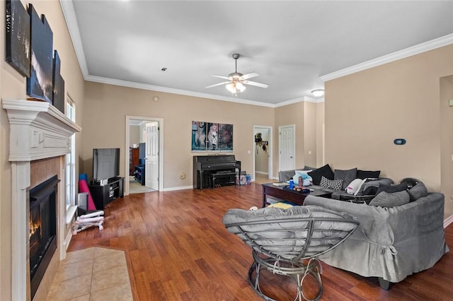 living room with a ceiling fan, crown molding, a lit fireplace, wood finished floors, and baseboards