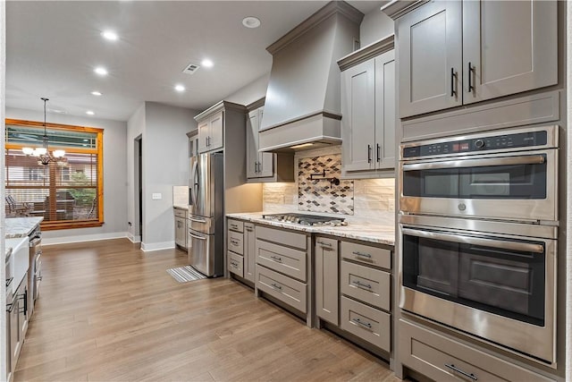kitchen featuring stainless steel appliances, premium range hood, gray cabinets, baseboards, and a chandelier