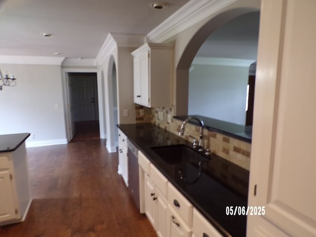 kitchen with dark countertops, crown molding, backsplash, a sink, and arched walkways