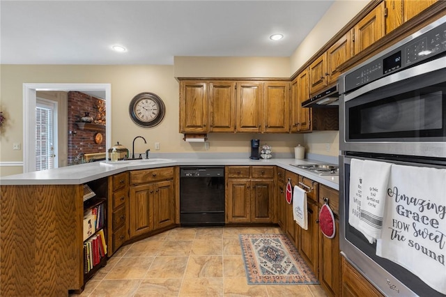 kitchen featuring appliances with stainless steel finishes, a sink, a peninsula, and brown cabinetry