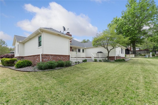 rear view of property featuring a yard, a wooden deck, brick siding, and a chimney