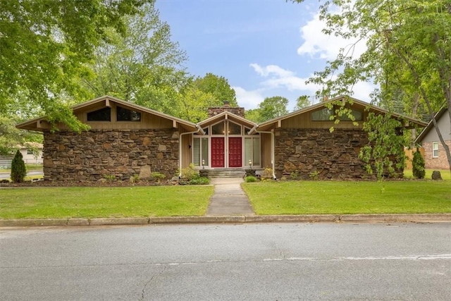 mid-century modern home featuring stone siding, a chimney, and a front yard