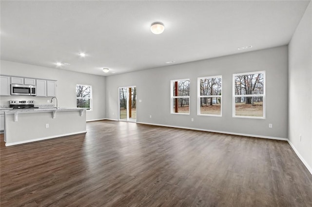 unfurnished living room featuring plenty of natural light, dark wood-style flooring, baseboards, a sink, and recessed lighting