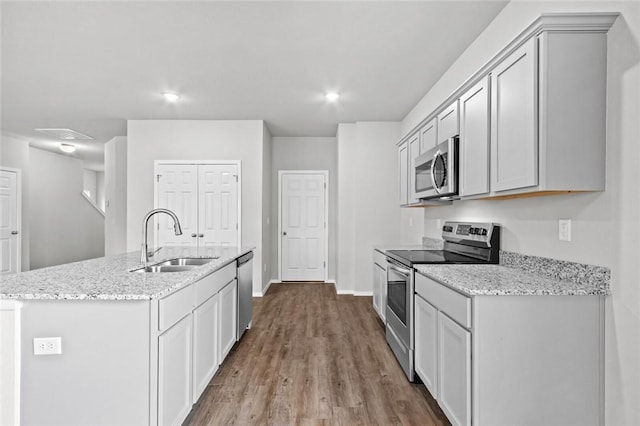 kitchen with stainless steel appliances, a sink, wood finished floors, light stone countertops, and recessed lighting