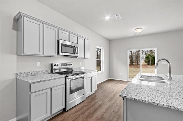 kitchen with appliances with stainless steel finishes, a sink, gray cabinets, dark wood-style flooring, and recessed lighting