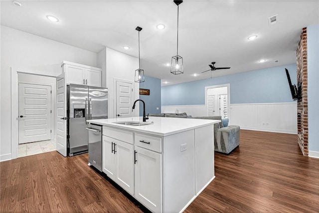kitchen with a sink, appliances with stainless steel finishes, a ceiling fan, dark wood-style flooring, and a wainscoted wall