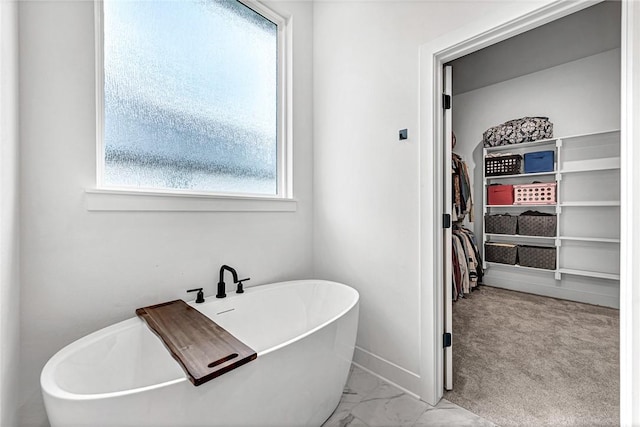 bathroom with a spacious closet, plenty of natural light, a freestanding bath, and marble finish flooring