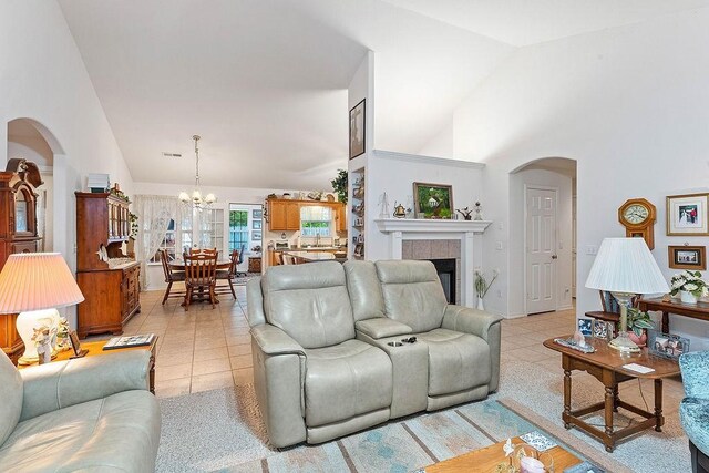 living area featuring arched walkways, a chandelier, high vaulted ceiling, a fireplace, and light tile patterned flooring
