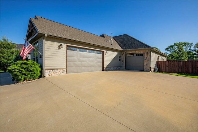 view of front facade with stone siding, fence, a garage, driveway, and roof with shingles