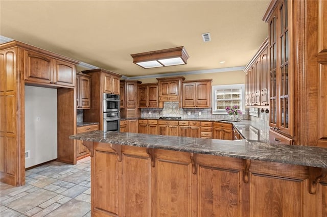 3907 NE Cadbury Ave, Bentonville, AR 72712 - kitchen with appliances with stainless steel finishes, backsplash, ornamental molding, brown cabinetry, and dark stone countertops