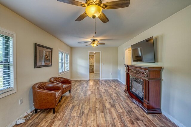 living area with wood finished floors, baseboards, a glass covered fireplace, and a ceiling fan