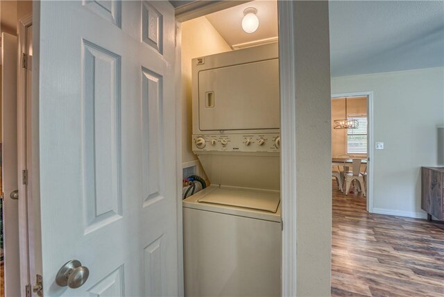 laundry room featuring estacked washer and dryer, wood finished floors, and baseboards