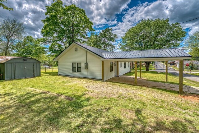 rear view of house featuring a shed, an outdoor structure, a yard, metal roof, and driveway