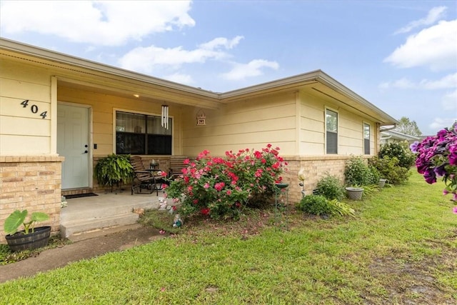 view of exterior entry featuring a porch, a lawn, and brick siding