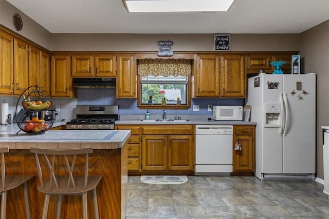 kitchen featuring white appliances, under cabinet range hood, and brown cabinetry