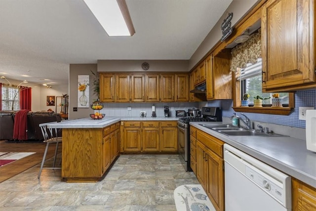 kitchen with white appliances, a sink, a peninsula, under cabinet range hood, and brown cabinets