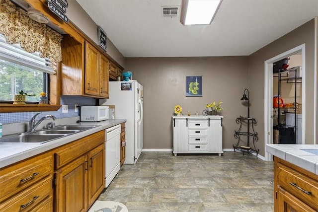 kitchen featuring white appliances, a sink, brown cabinets, baseboards, and stone finish floors