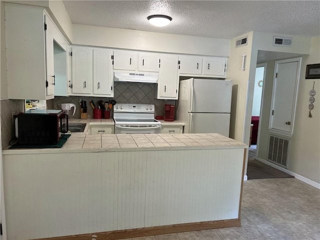 kitchen with white appliances, under cabinet range hood, a peninsula, tasteful backsplash, and white cabinets