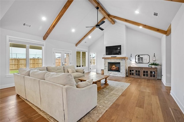 living room featuring beamed ceiling, ceiling fan, baseboards, a warm lit fireplace, and wood finished floors