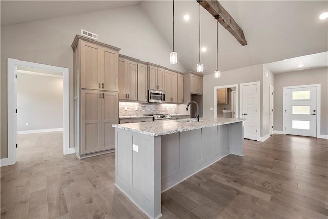 kitchen featuring stainless steel microwave, a sink, a kitchen island with sink, range, and decorative backsplash