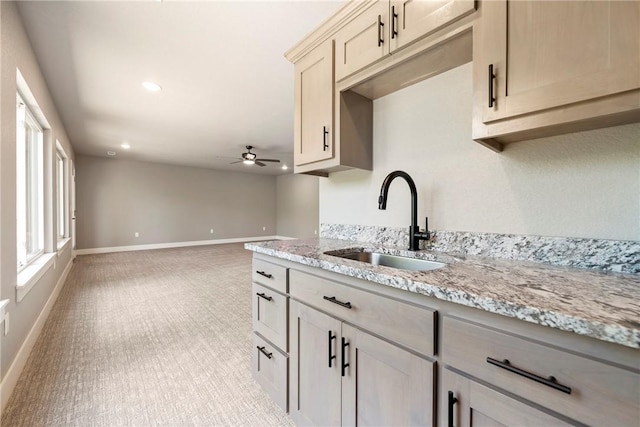 kitchen with a sink, light carpet, a ceiling fan, baseboards, and light stone countertops