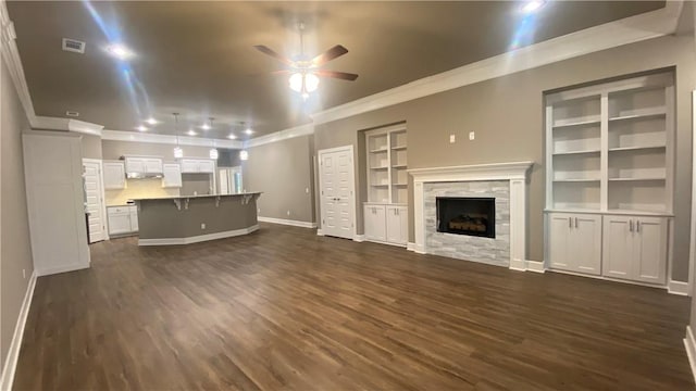 unfurnished living room with ornamental molding, ceiling fan, dark wood-type flooring, baseboards, and a fireplace