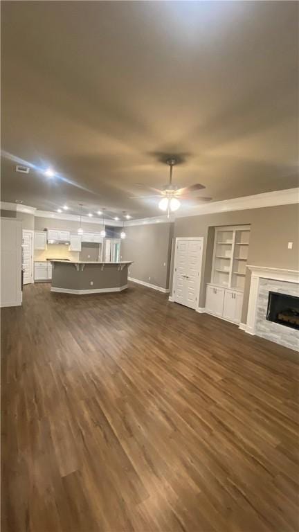 unfurnished living room with dark wood-style flooring, a fireplace, built in shelves, baseboards, and ornamental molding