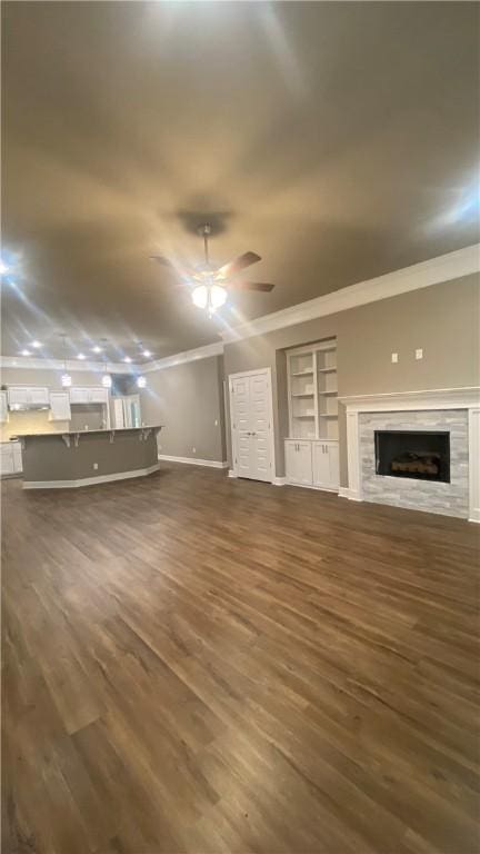 unfurnished living room with wood finished floors, crown molding, a premium fireplace, baseboards, and ceiling fan