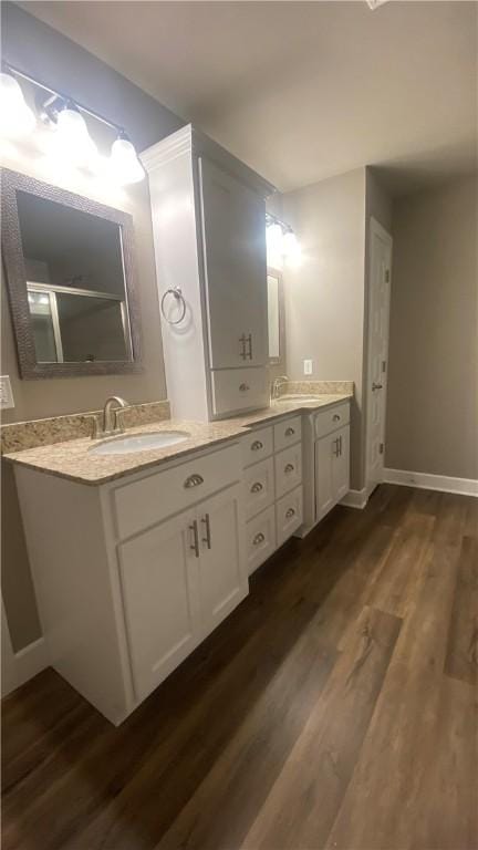 full bath featuring wood finished floors, double vanity, and baseboards