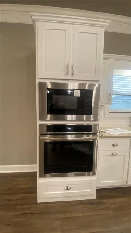 kitchen view of stainless steel oven, built in microwave, white cabinets, and dark wood-style floors