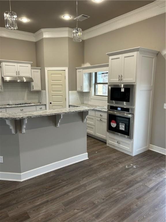 kitchen featuring stainless steel appliances, ornamental molding, under cabinet range hood, white cabinetry, and a chandelier