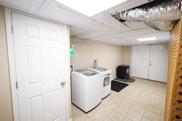 clothes washing area with a wood stove, separate washer and dryer, and light tile patterned floors