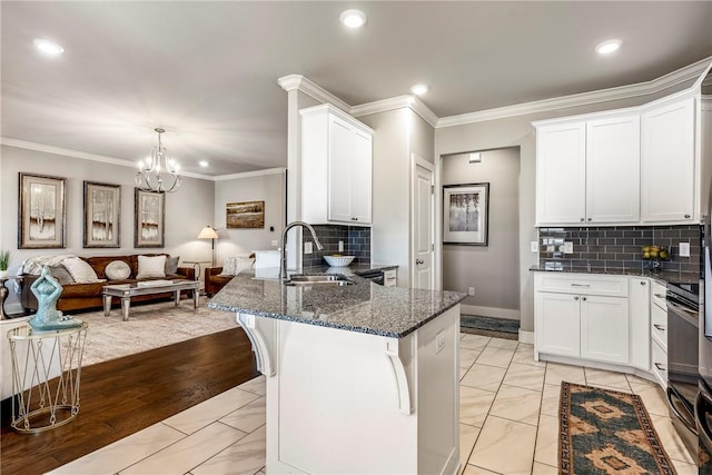 kitchen with a sink, dark stone counters, crown molding, white cabinets, and open floor plan