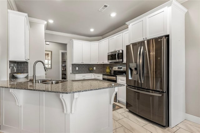 kitchen with appliances with stainless steel finishes, a sink, a peninsula, dark stone counters, and ornamental molding