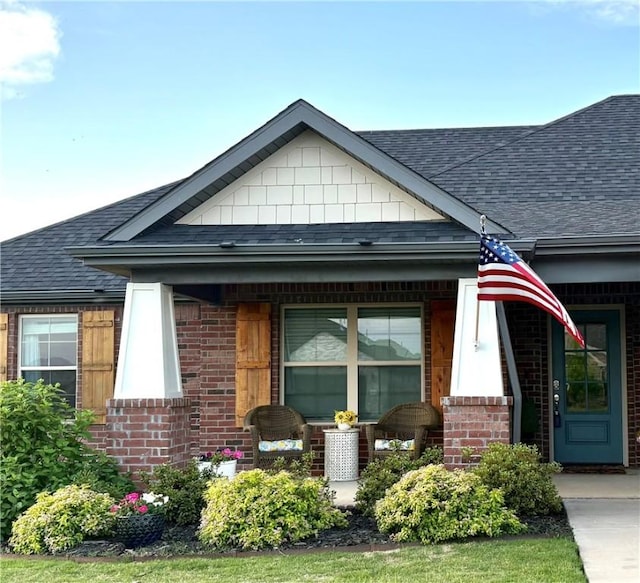 view of front of house with roof with shingles, brick siding, and covered porch
