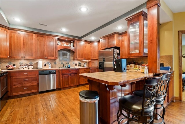 30 Brittany Ln, Bella Vista, AR 72714 - kitchen with appliances with stainless steel finishes, a breakfast bar, a peninsula, glass insert cabinets, and light wood-style flooring