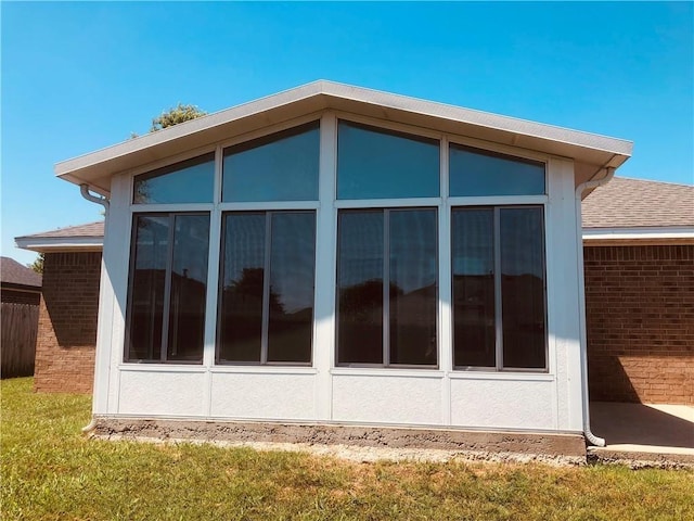 view of side of property with brick siding, a sunroom, and roof with shingles