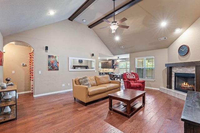 living area featuring ceiling fan, arched walkways, wood finished floors, baseboards, and beam ceiling