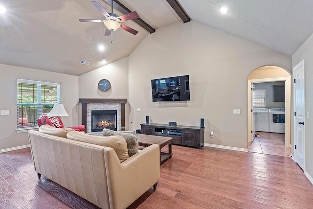 living area with separate washer and dryer, a ceiling fan, a stone fireplace, baseboards, and beam ceiling